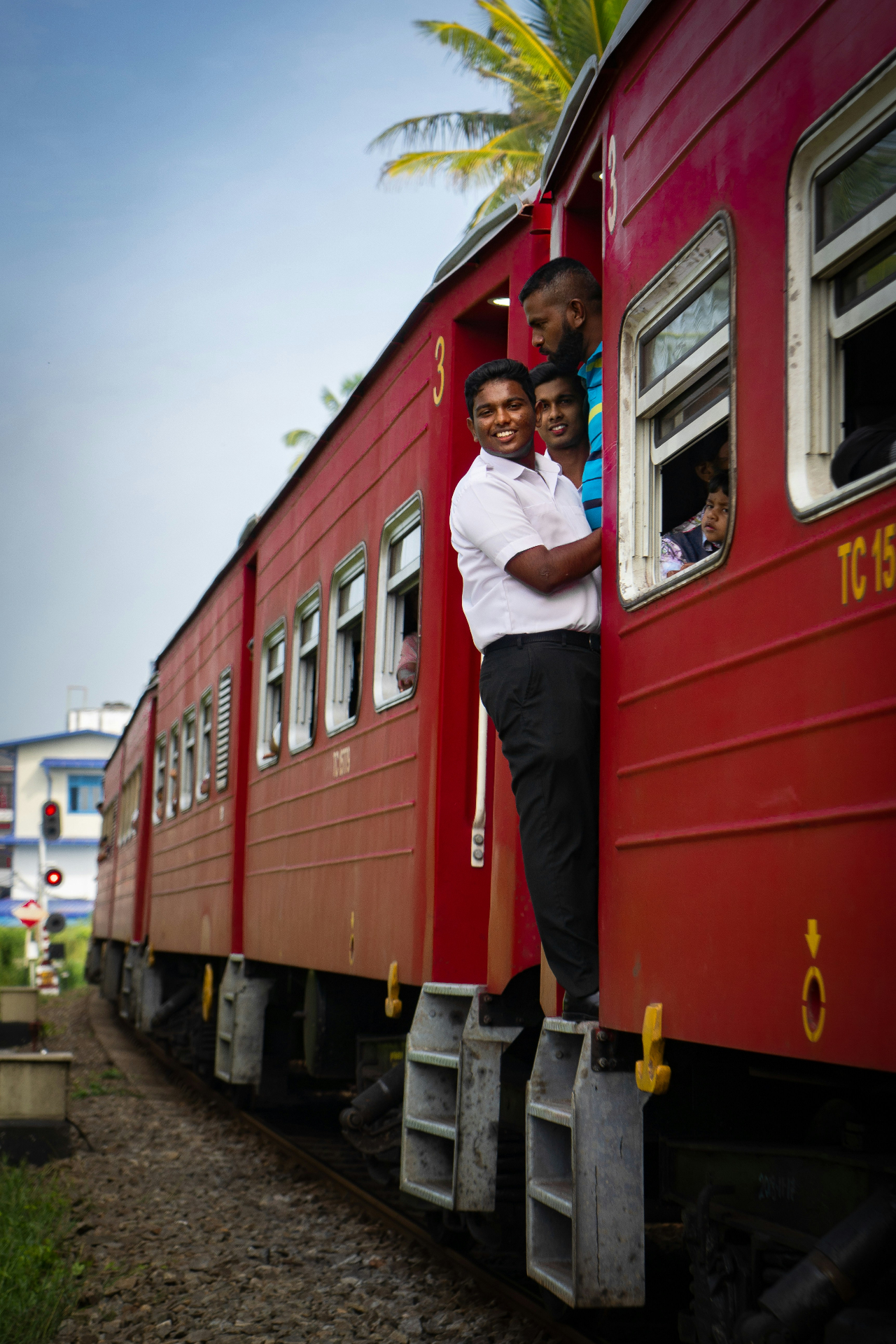 Passengers on a vibrant red Sri Lankan train with palm trees